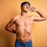 Young handsome man shirtless wearing swimsuit and swim cap over